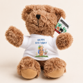 A brown plush teddy bear wearing a white short-sleeve T-shirt with a blue 'HAPPY BIRTHDAY' graphic and cartoon bear illustration. The bear has a black nose and embroidered eyes, with a 'SOWMENT' brand tag attached to its ear, set against a plain beige background.