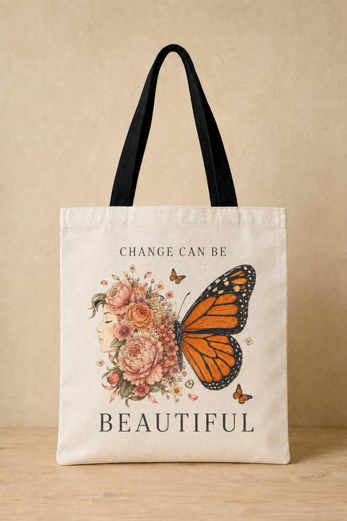 An off-white canvas tote bag with black shoulder straps, featuring a printed design of an orange monarch butterfly, pink flowers, and the text 'CHANGE CAN BE BEAUTIFUL' on a beige background.