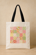 An off-white canvas tote bag with black shoulder straps, featuring a colorful patchwork-style square print on the front with floral, striped, and polka-dot patterns in pink, green, yellow, and orange, set against a neutral beige background.