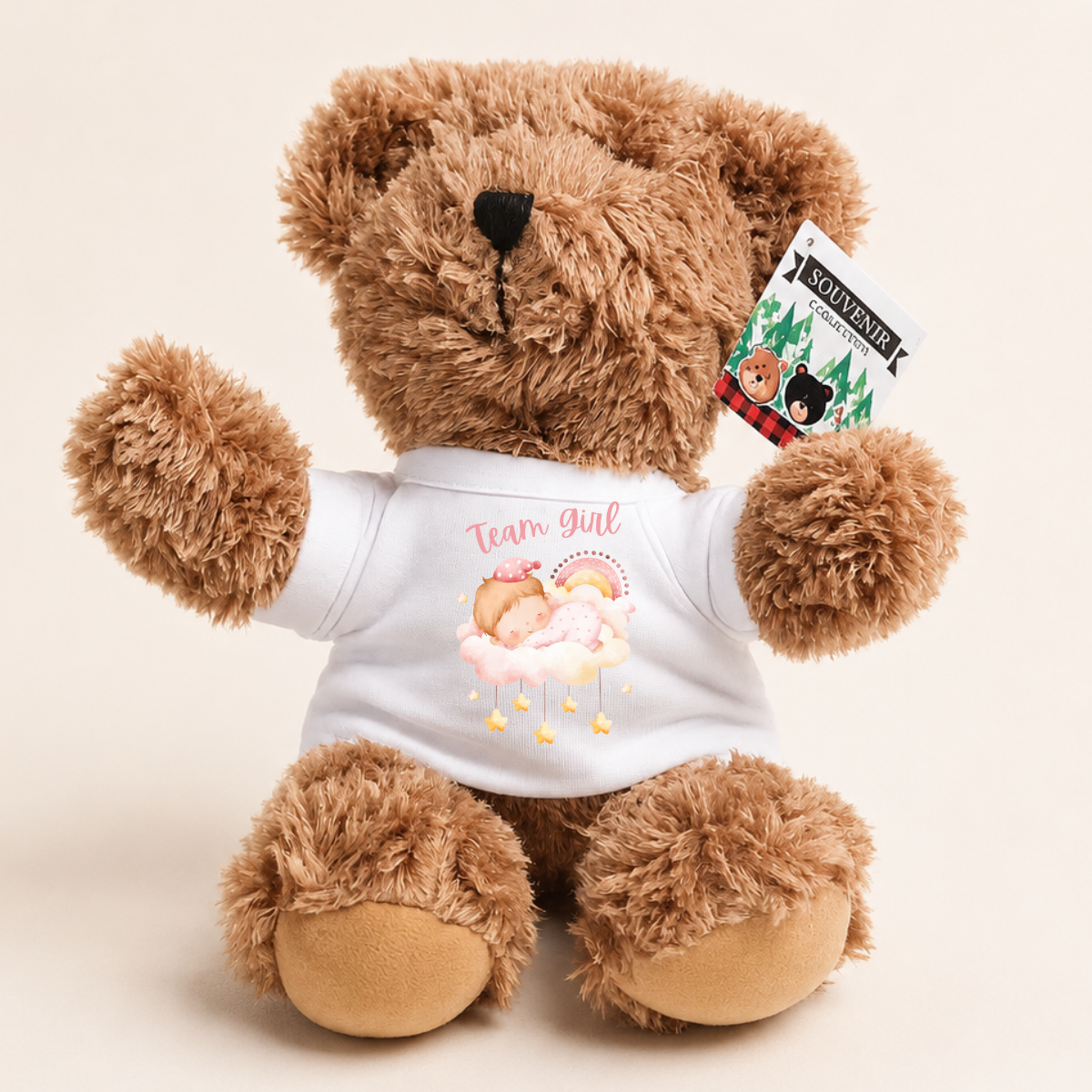 A brown plush teddy bear wearing a white T-shirt with a pink and yellow 'Team Girl' graphic, shown against a light beige background. A hangtag on the ear reads 'SOWLAND'.