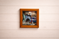 Framed artwork with a collage of various elements on a light wooden panel background