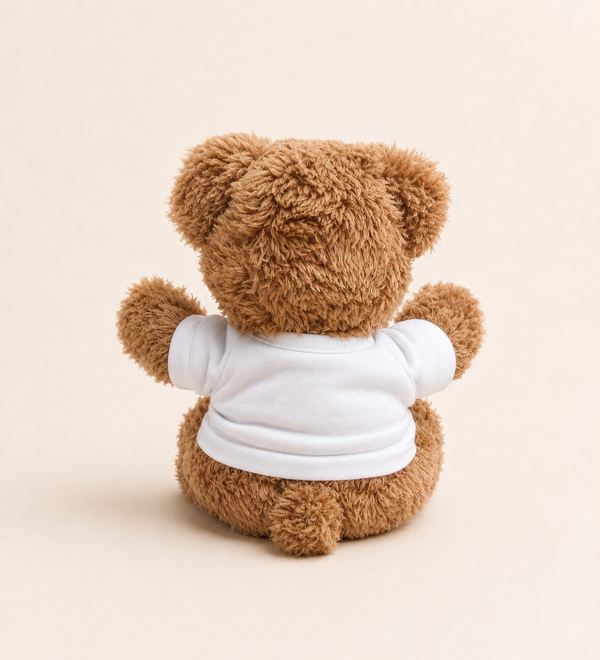 A brown plush teddy bear viewed from the back, wearing a plain white short-sleeve shirt, centered on a warm cream background.