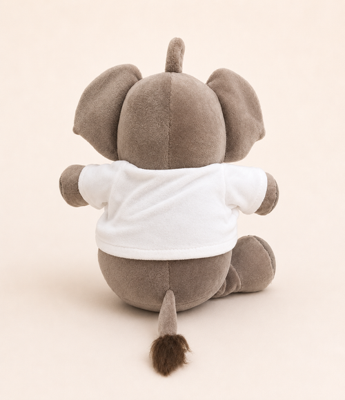 A plush elephant toy shown from the back, wearing a plain white short-sleeve shirt, set against a solid light beige background.