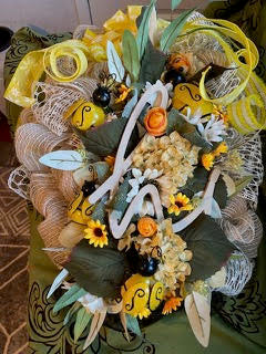 Decorative wreath with yellow ribbons, flowers, and decorative elements on a textured surface.