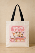 An off-white canvas tote bag with black shoulder straps, featuring a cute illustration of a sleeping cat on books next to a coffee mug under a pink cloud that reads 'BOOKS, CATS & COFFEE'.