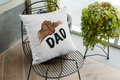 Decorative pillow with 'DAD' and hand graphic on a black wire chair with plants in the background.