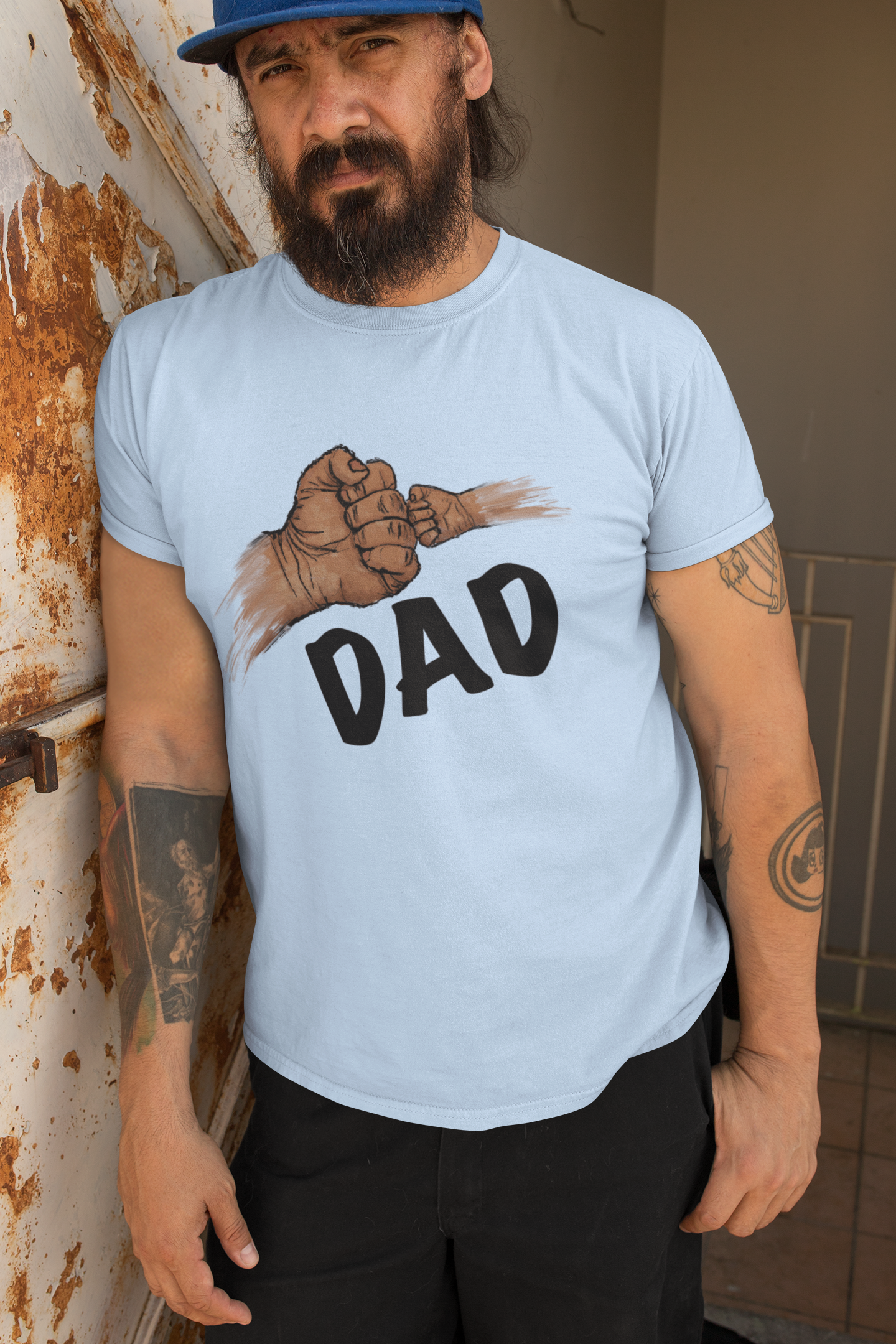 Man wearing a light blue t-shirt with a graphic and 'DAD' text, standing against a wall.