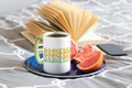 White mug with 'DANCE DAD' text on a saucer with fruit and a phone, on a textured surface.
