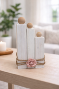 Decorative arrangement of white cylindrical blocks with wooden spheres and a pink flower on a wooden surface.