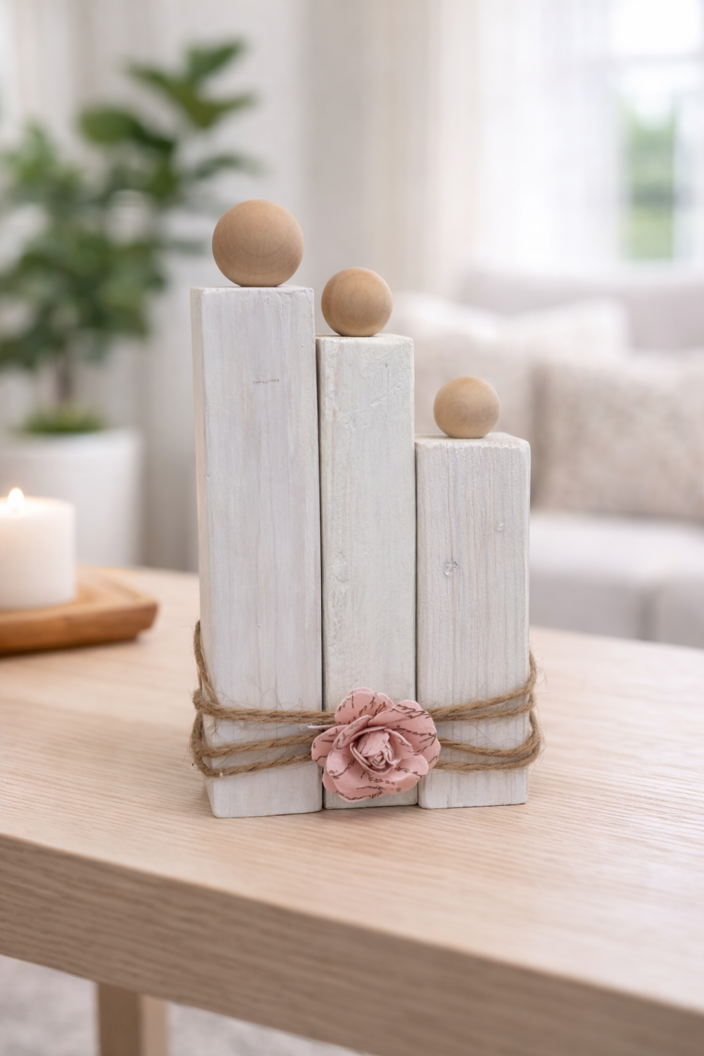 Decorative arrangement of white cylindrical blocks with wooden spheres and a pink flower on a wooden surface.