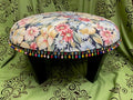 Decorative stool with floral pattern and colorful tassels on a green fabric background