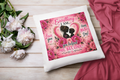Decorative pillow with floral design and text on a wooden surface with flowers and fabric.