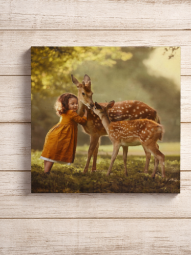 Canvas print of a girl in an orange dress interacting with two deer in a natural setting.