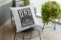 Pillow with 'Greatest Dad' text on a black wire chair with plants in the background