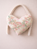 Heart-shaped pillow with floral pattern and rope handle on a light background