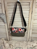 Floral-patterned bag with a black strap hanging on a wooden door.