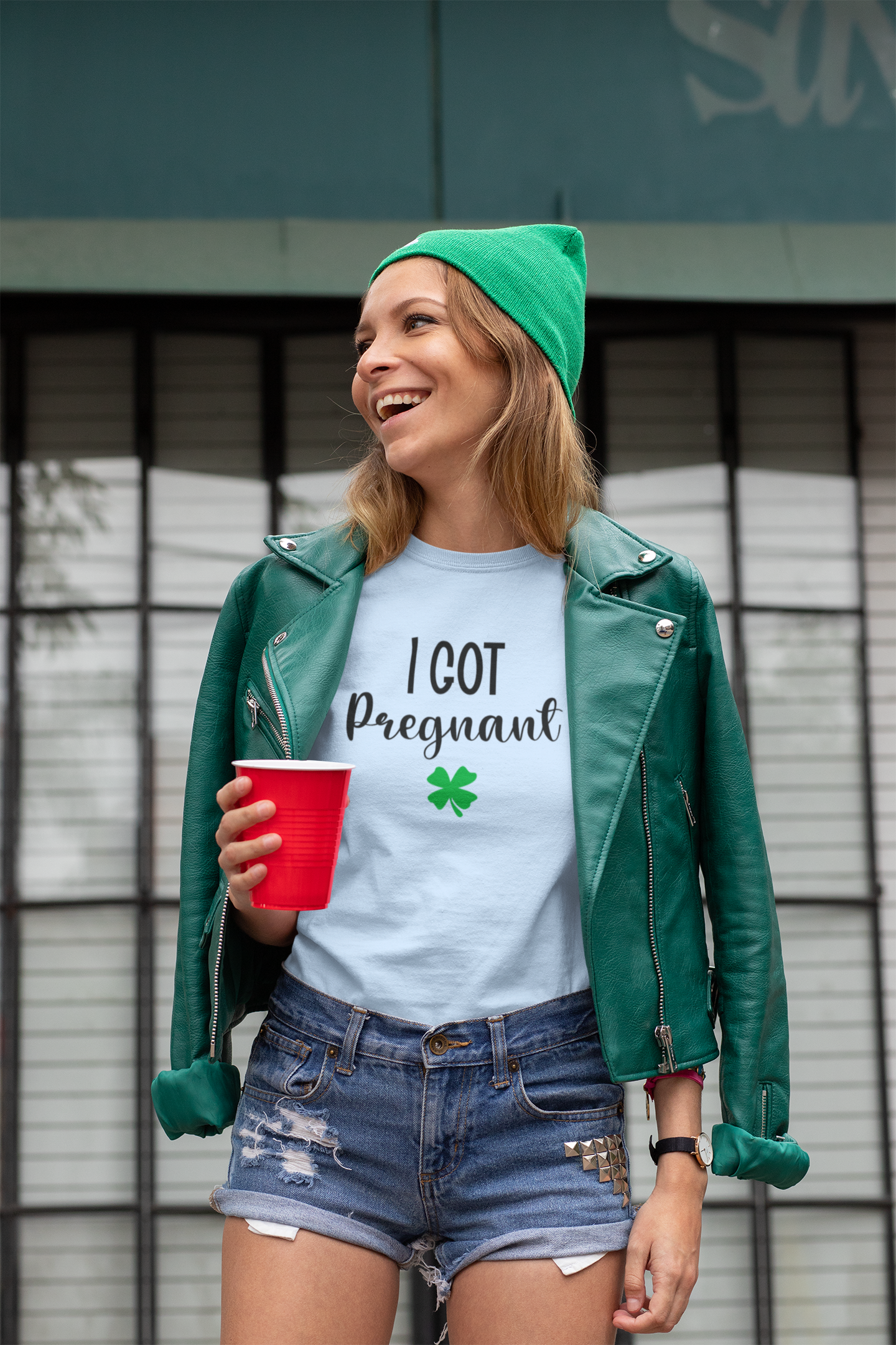 Woman wearing a green beanie and leather jacket, holding a red cup, with blue tee
