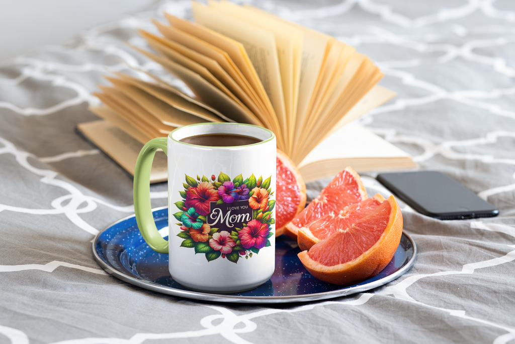 Mug with floral design and 'Mom' text on a saucer with fruit and phone, on a textured surface.