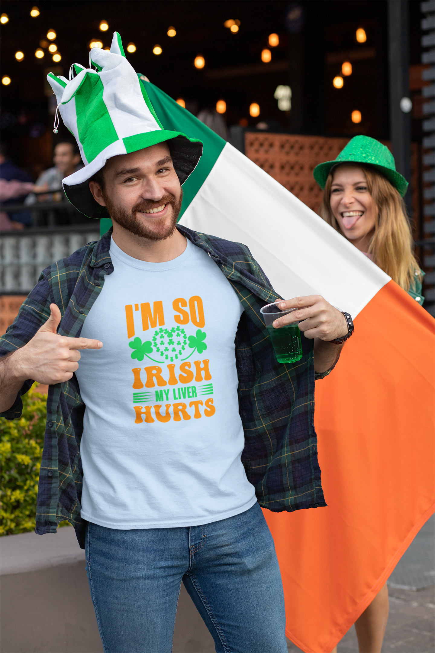 Man wearing a blue t-shirt with 'I'm so Irish my liver hurts' text, holding an Irish flag, and pointing at himself.