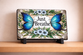 Decorative plaque with butterflies and flowers on a stand against a beige wall.