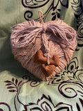 Heart-shaped pink yarn ball with a small brown object on a patterned fabric background