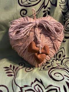 Heart-shaped pink yarn ball with a small brown object on a patterned fabric background