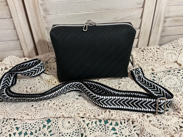 Black textured handbag with a black and white patterned strap on a textured surface.