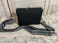 Black textured handbag with a black and white patterned strap on a textured surface.