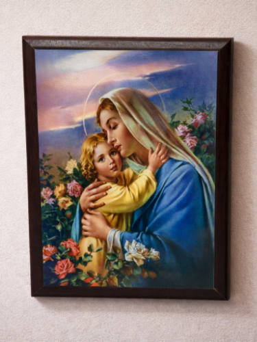 Framed artwork of a woman holding a child amidst flowers and a scenic background.