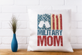 Pillow with 'Military Mom' text and American flag design on a white brick wall background