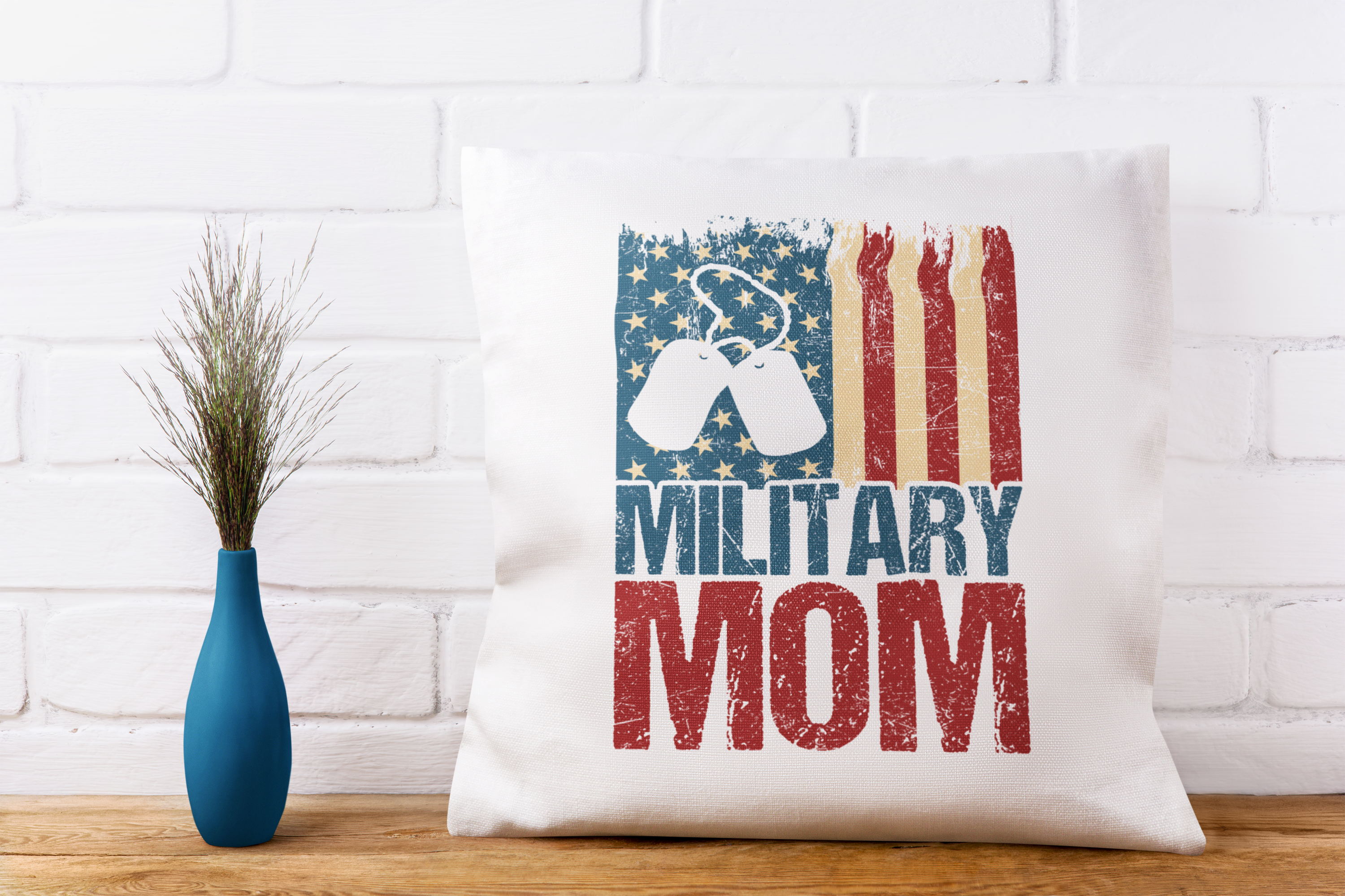 Pillow with 'Military Mom' text and American flag design on a white brick wall background