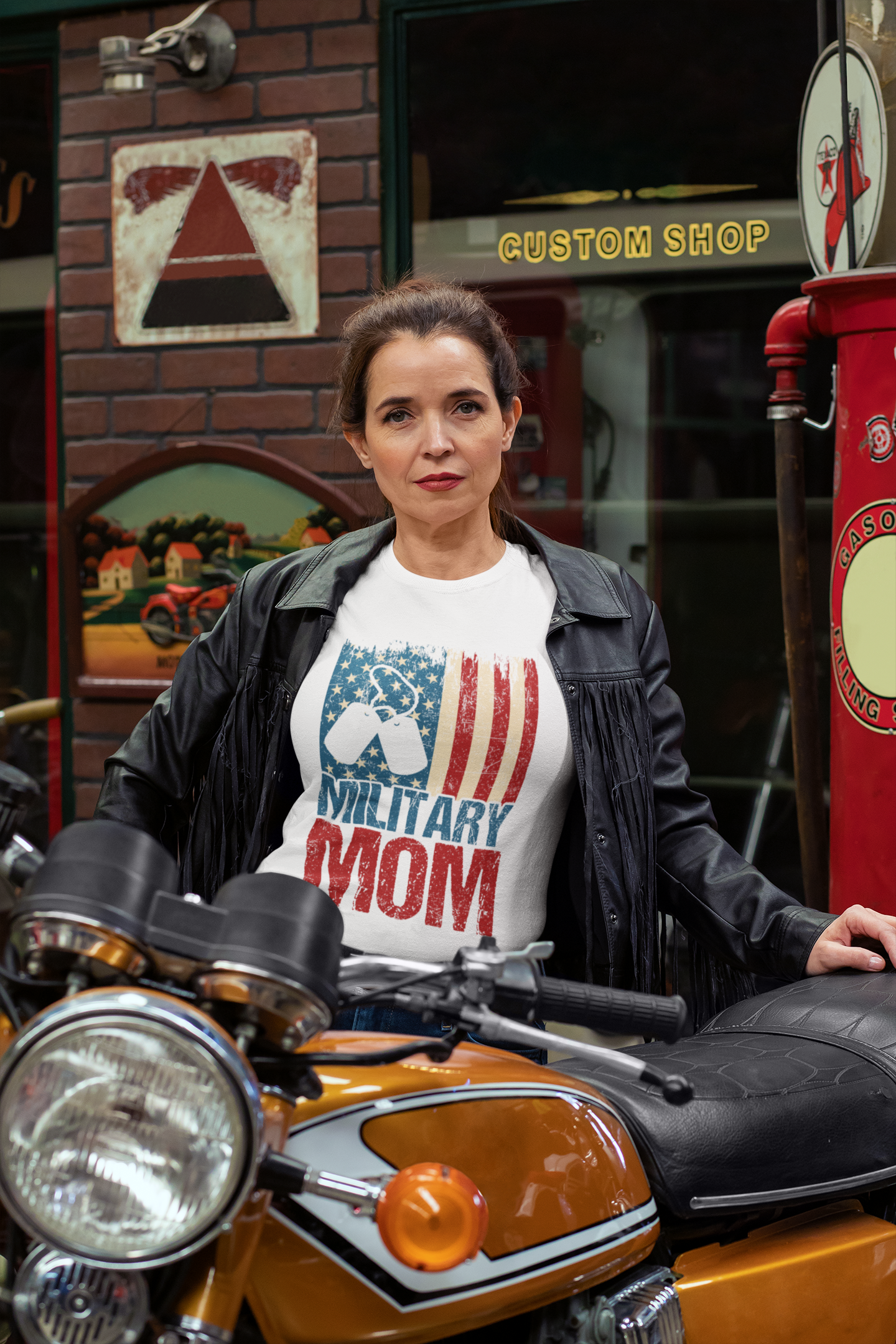 Woman wearing a 'Military Mom' t-shirt sitting on a motorcycle in front of a vintage store.