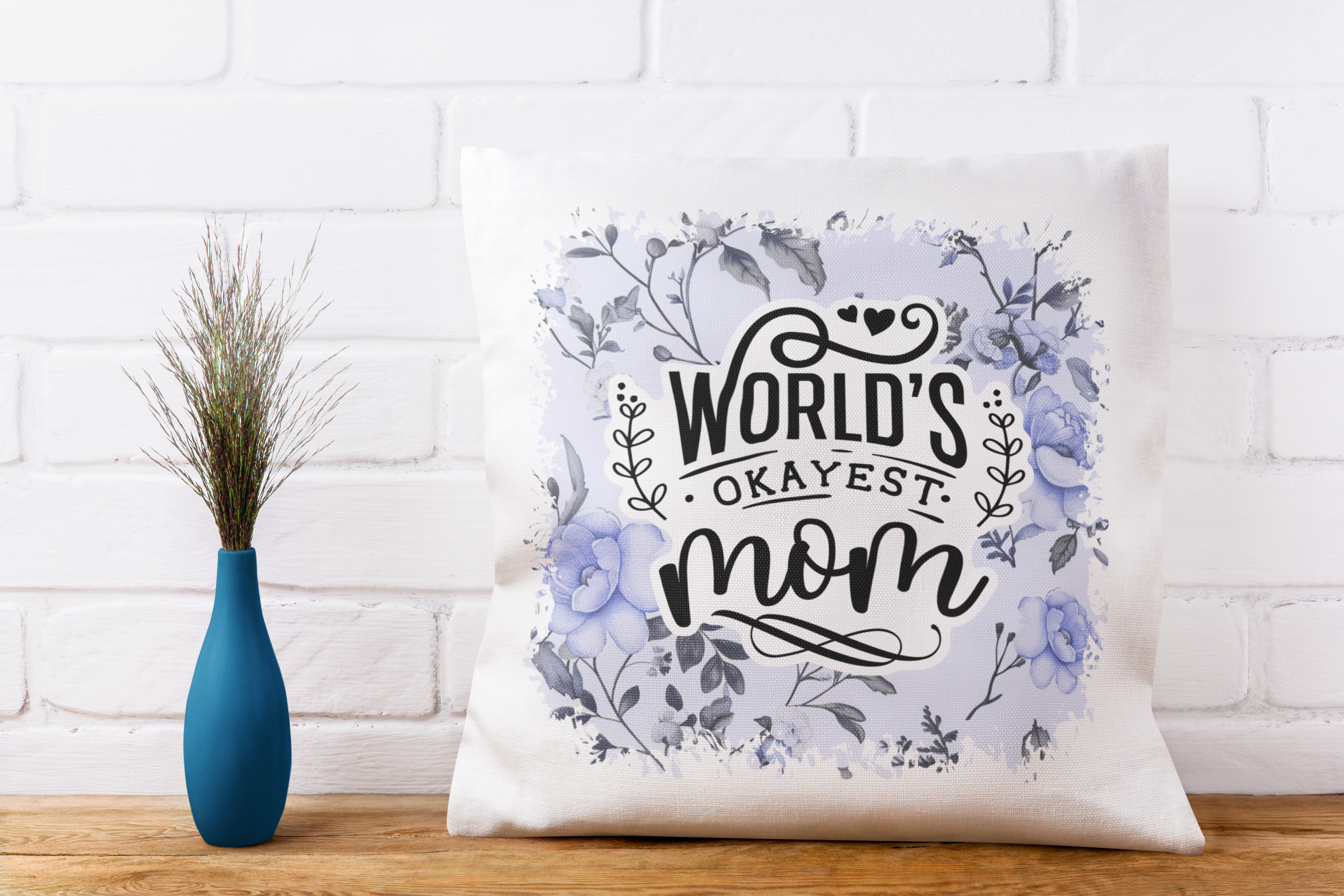 Decorative pillow with 'World's Okayest Mom' text on a white brick wall background