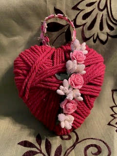 Heart-shaped yarn craft with pink flowers on a patterned fabric background