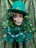 Decorative figure with green attire and accessories against a patterned curtain background