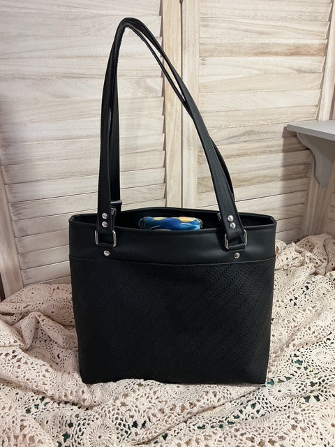 Black handbag with a textured surface on a wooden floor.