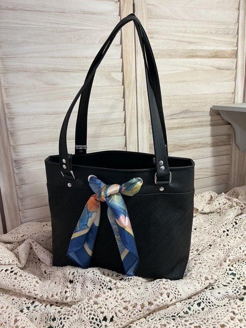 Black handbag with a colorful scarf draped over it on a wooden surface.