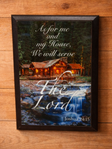 Framed print with a scenic landscape and religious text on a wooden surface