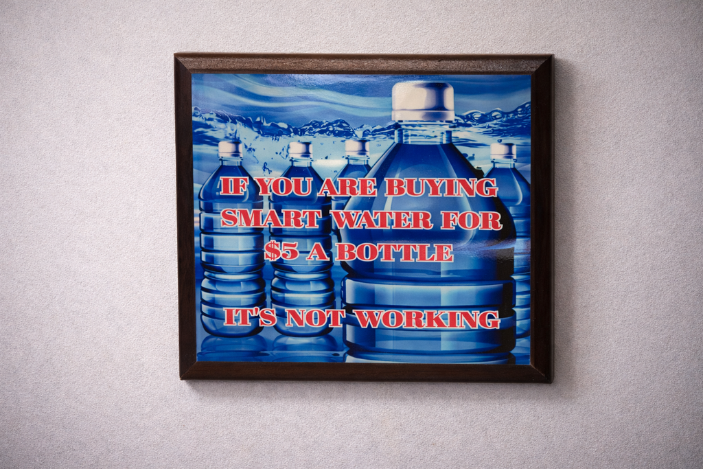 Framed poster with blue water bottles and text on a gray wall