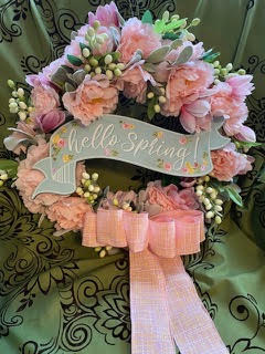 Decorative wreath with pink flowers, greenery, and a 'hello Spring!' sign on a patterned background.