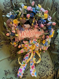 Decorative wreath with flowers and a 'Welcome' sign on a patterned background