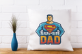 Pillow with 'Super Dad' design on a white brick wall background