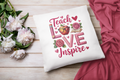White pillow with 'Teach Love Inspire' text and floral designs on a wooden surface with flowers and fabric.
