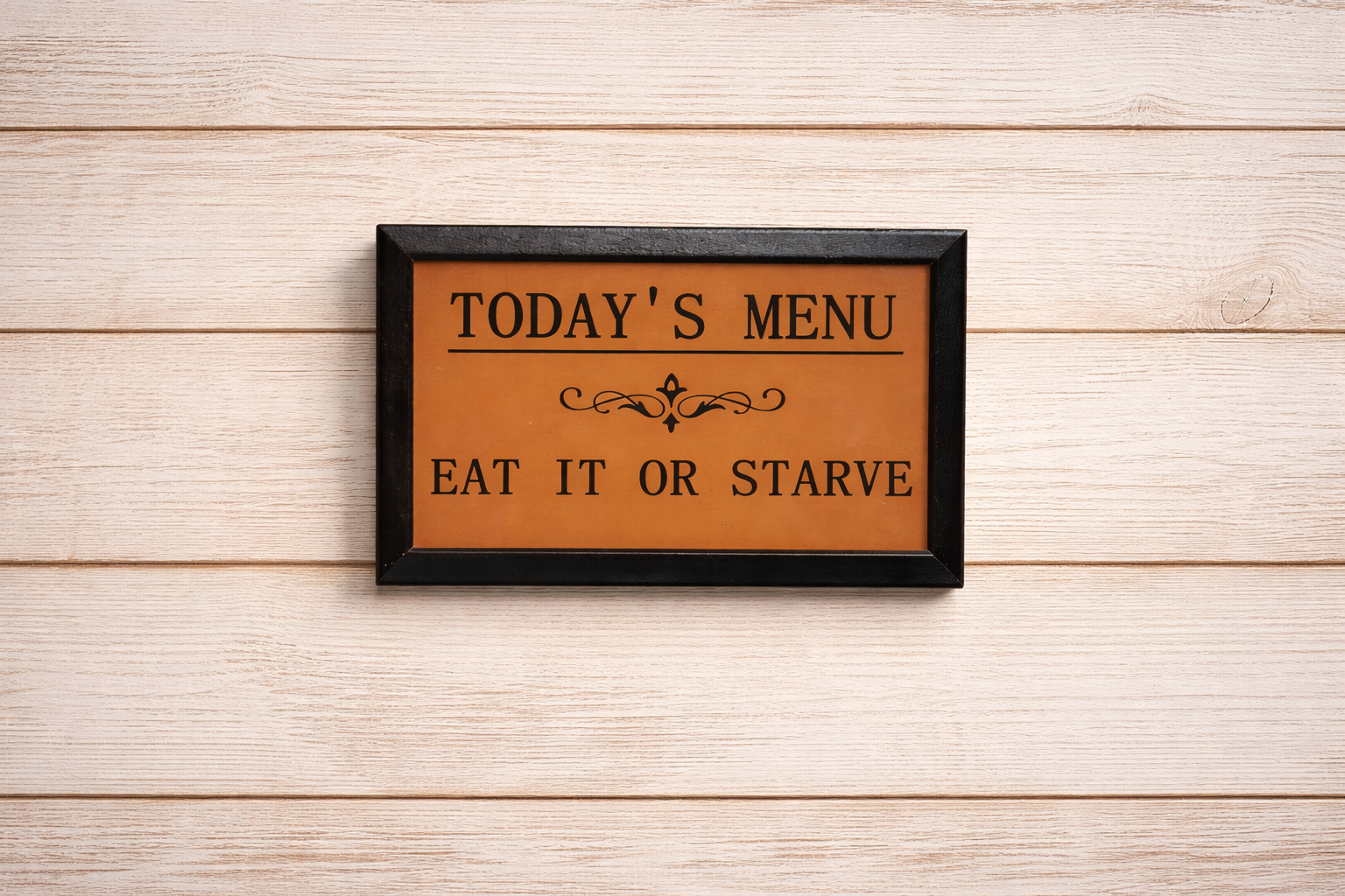 Framed sign with 'Today's Menu: Eat It or Starve' text on a wooden background