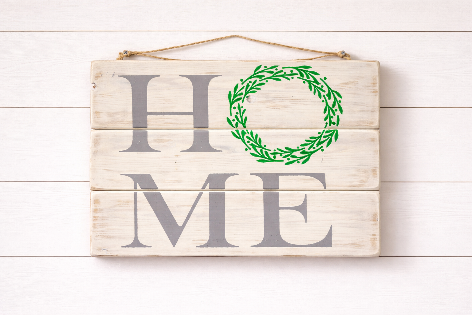 Wooden sign with 'HOME' and green wreath on a white wooden background